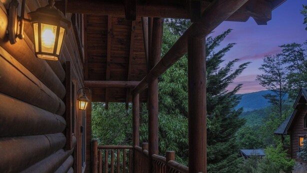 A wooden cabin with a porch, a lantern, and a view of the surrounding forest. - Budget friendly, Smoky Mountain Cabin Rental | Sleeps 10 | Pool Table (Pigeon Forge)