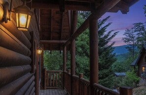 A wooden cabin with a porch, a lantern, and a view of the surrounding forest. - Budget friendly, Smoky Mountain Cabin Rental | Sleeps 10 | Pool Table (Pigeon Forge)