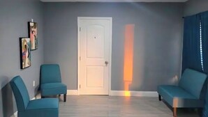 Una habitación con dos sillones azules, una puerta blanca y un suelo de madera claro.