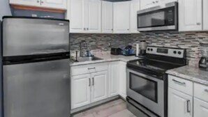 Una cocina con armarios blancos, un refrigerador de acero inoxidable, un microondas y una estufa.