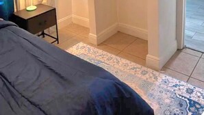 Un dormitorio con cama, una mesita de noche con lámpara, un armario con perchero y vistas a un balcón.