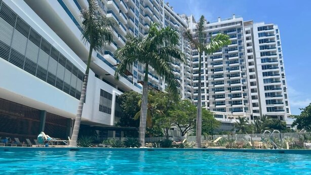 Ein Hotel mit Swimmingpool, Palmen und hoch aufragenden Gebäuden im Hintergrund.