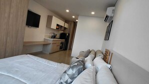 Ein Schlafzimmer mit Bett, Kissen, Fernseher, einer Küchenzeile und einer Klimaanlage.
