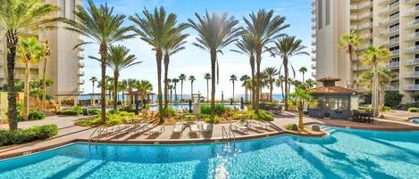 A swimming pool surrounded by palm trees and a building with balconies.