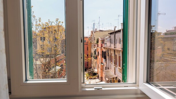 Ein Fenster mit Blick auf eine enge, von Häusern gesäumte Straße, einer sichtbaren Treppe und einen Baum mit gelben Blättern.