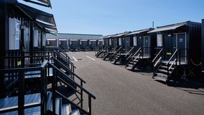 A row of portable cabins with individual numbers, a clear sky, and a paved ground. - HOTEL R9 The Yard Nagahamainter (Nagahama)