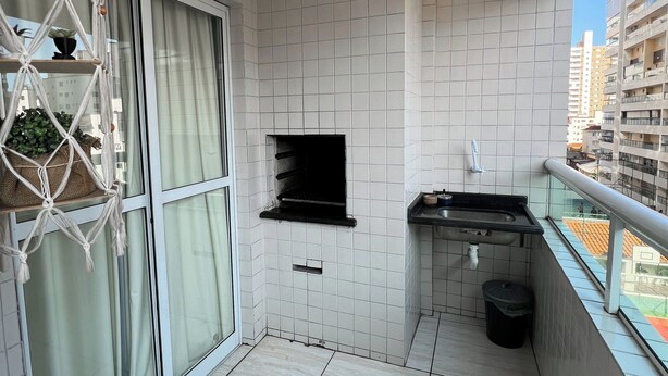 En balkong med ett kaklat golv, ett litet handfat, en papperskorg och en hylla i makramé med växter.