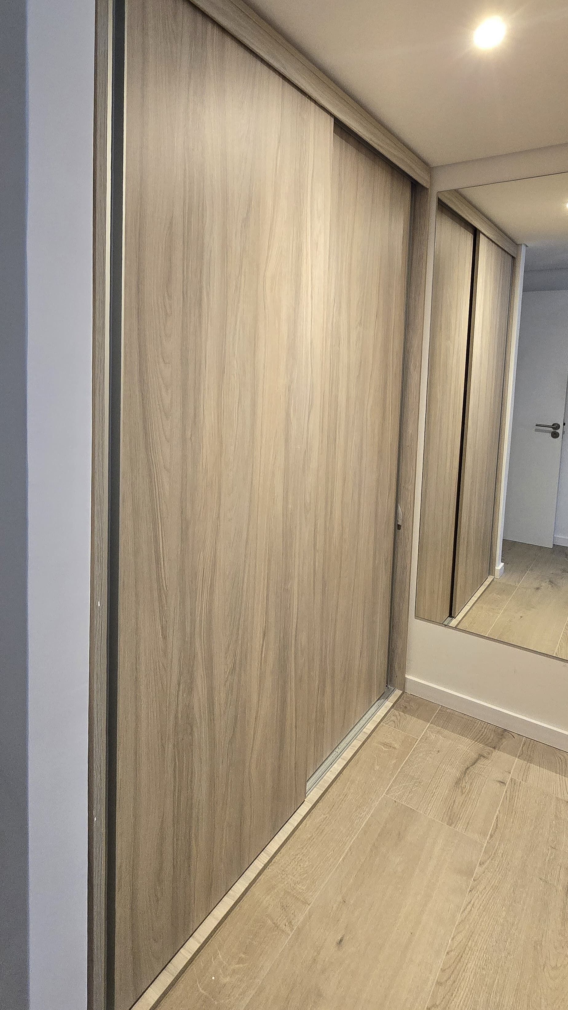 Um quarto com piso de madeira, um espelho grande e uma porta.