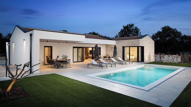 Een modern huis met een zwembad, terras en een verzorgd gazon.