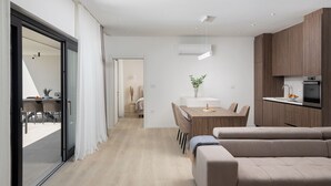 Een moderne, goed verlichte woonruimte met een bank, eettafel en keukenhoek.