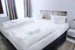 A double bed with white linens, a wooden headboard, and a bedside table with a drawer.