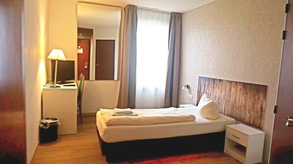A hotel room with a bed, bedside table, lamp, and a view of the outside. - Comfort Hotel Leipzig West (Schkeuditz)