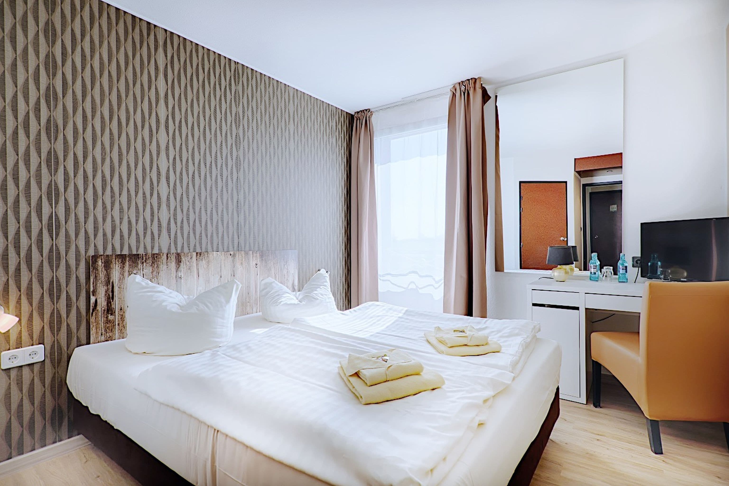 Ein Hotelzimmer mit einem großen Bett, einem Schreibtisch, einem Sessel und einem Fernseher.