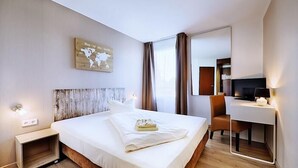 Una habitació d'hotel amb un llit, una taula de treball, una cadira, un mapa a la paret i una televisió.