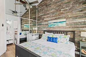 Ein Schlafzimmer mit Holzwand, einem Bett mit floralem Überwurf, einem Deckenventilator und einem Nachttisch mit Lampe.