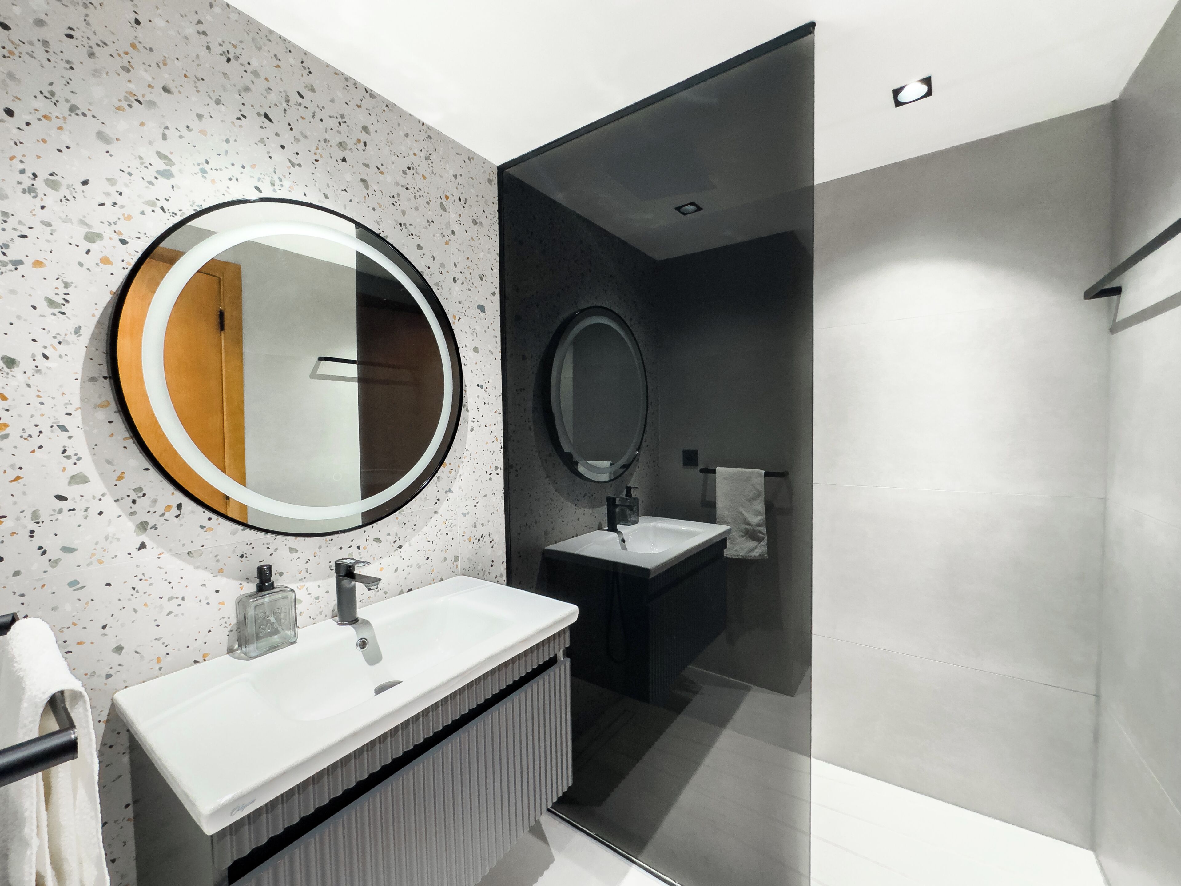 A modern bathroom with a round mirror, two sinks, and a shower area.
