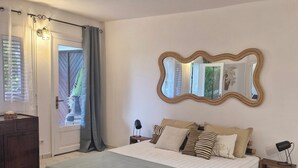 Un dormitorio con cama, mesita de noche, espejo, puerta y ventana.