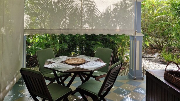 Un patio cubierto con una mesa y sillas, un mantel estampado y vistas de vegetación exuberante.