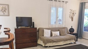 Un dormitorio con cama, televisor sobre un aparador de madera, ventana con cortinas y suelo de baldosas hexagonales.