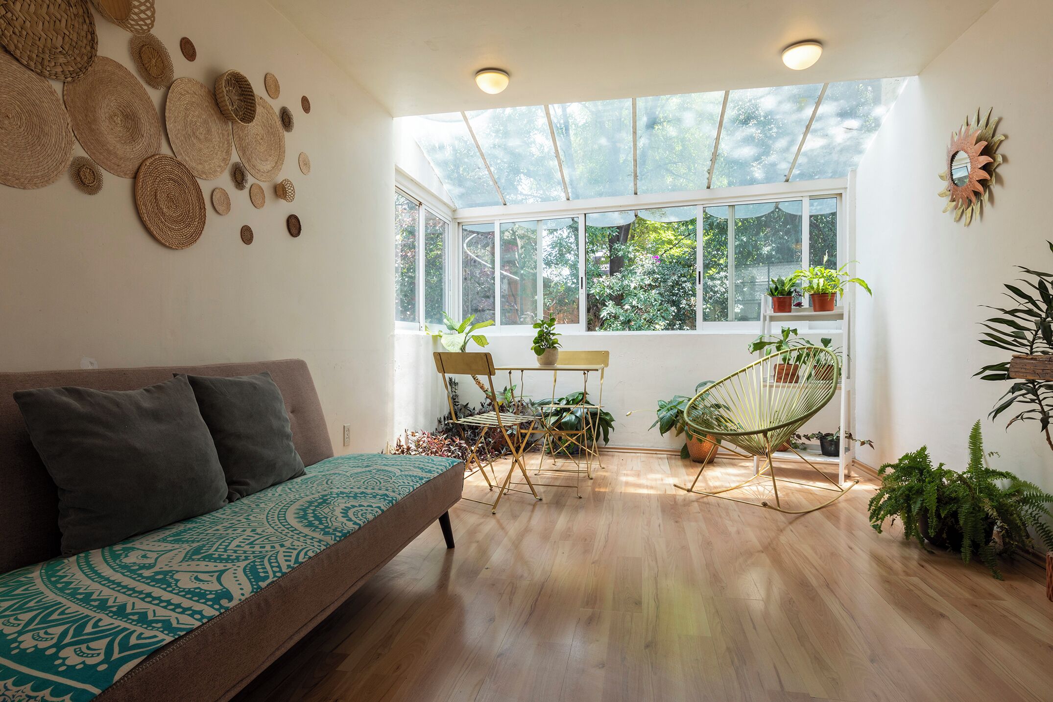 Ein Zimmer mit einer Couch, einem Sessel, einem Tisch mit Pflanzen und einem großen Fenster mit Blick auf Bäume.