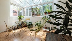 Ein Zimmer mit Holzboden, Glastür, einem Stuhl, einem Tisch und Topfpflanzen.