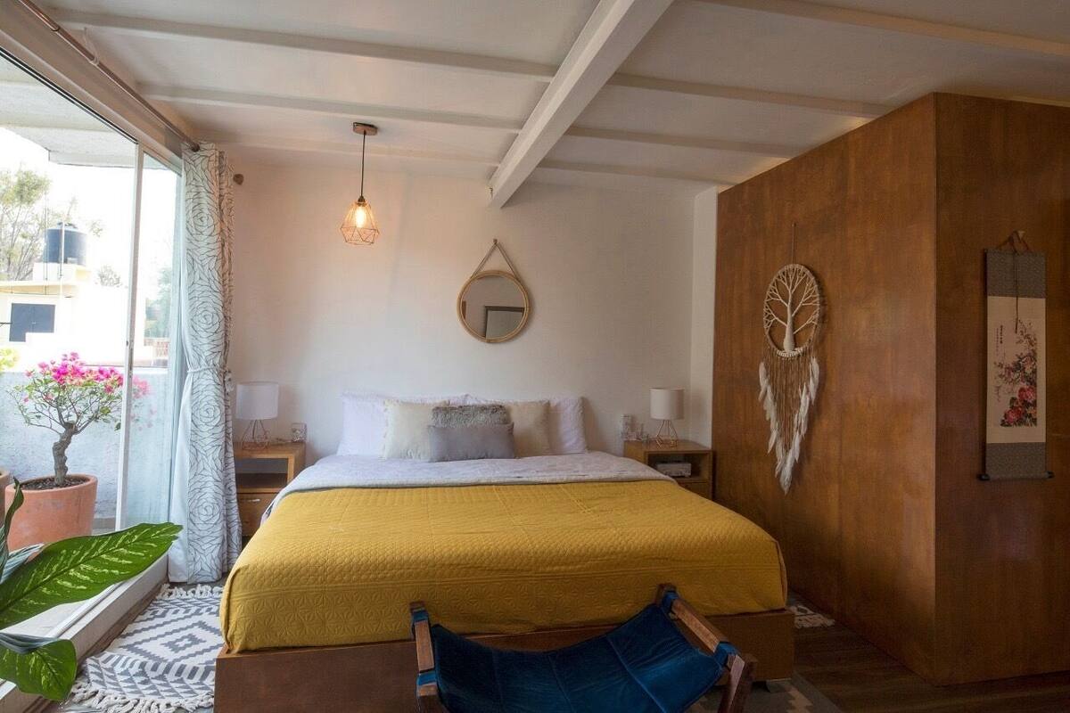 A bedroom with a bed, bedside tables, a hanging light fixture, a mirror, and a wall decoration.