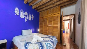 Ein Schlafzimmer mit blauer Wand, Holzboden und einem Bett mit gemusterten Bettbezügen.