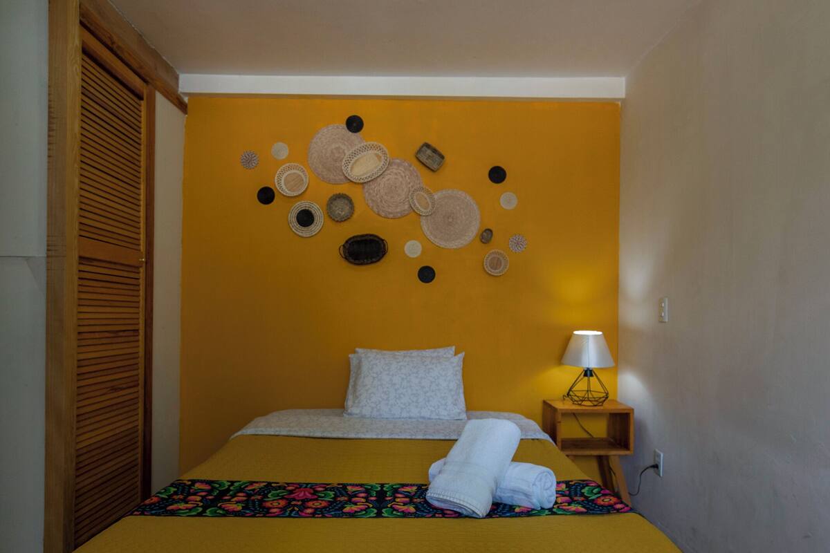 A room with a bed, a bedside table with a lamp, and a wall decoration.