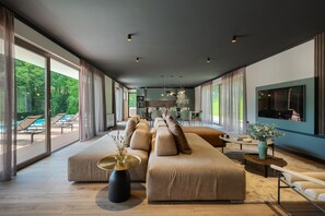 Een moderne woonkamer met een grote bank, een eethoek en een keuken op de achtergrond.