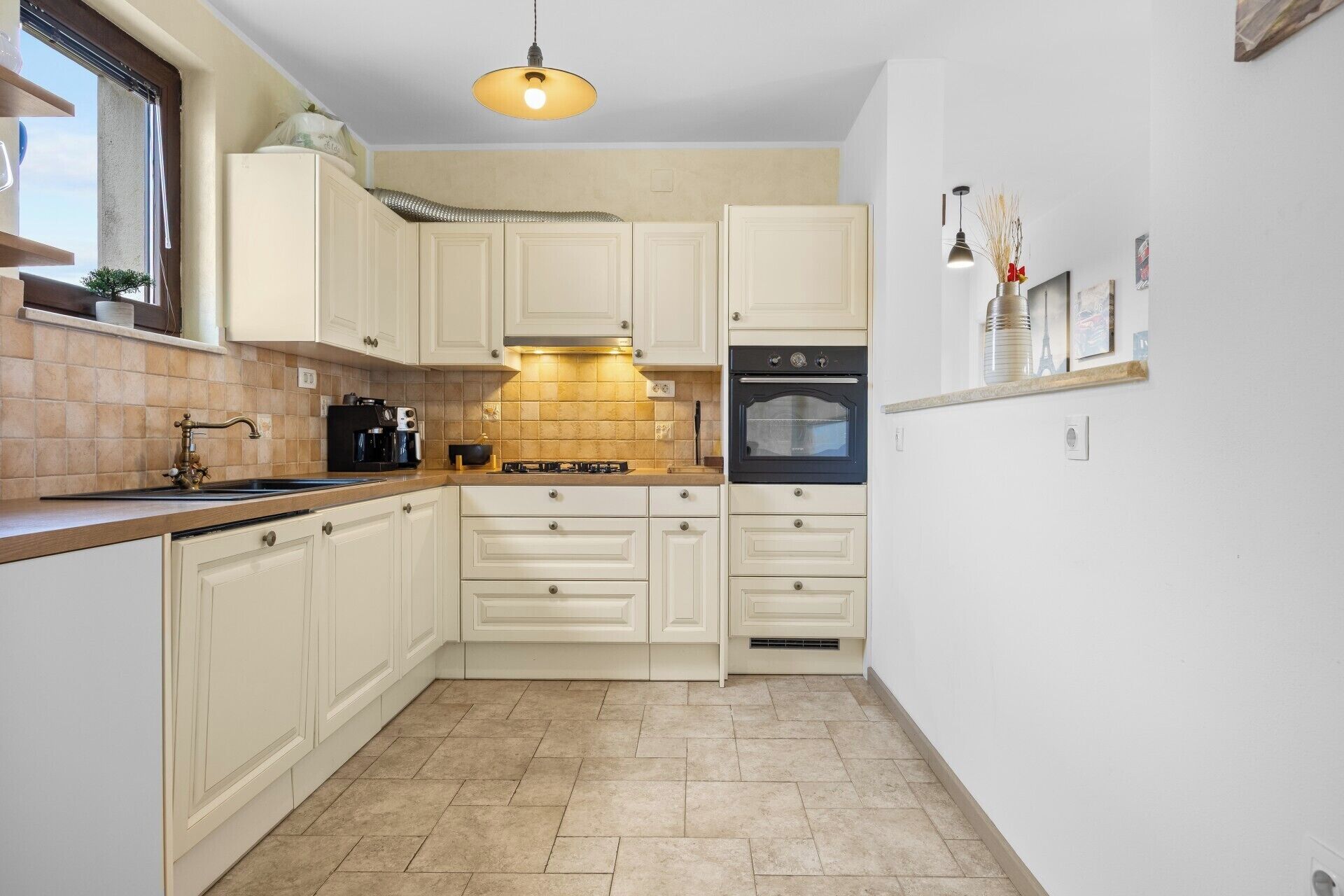 A compact kitchen with white cabinets, a black oven, a coffee maker, and a hanging light fixture.