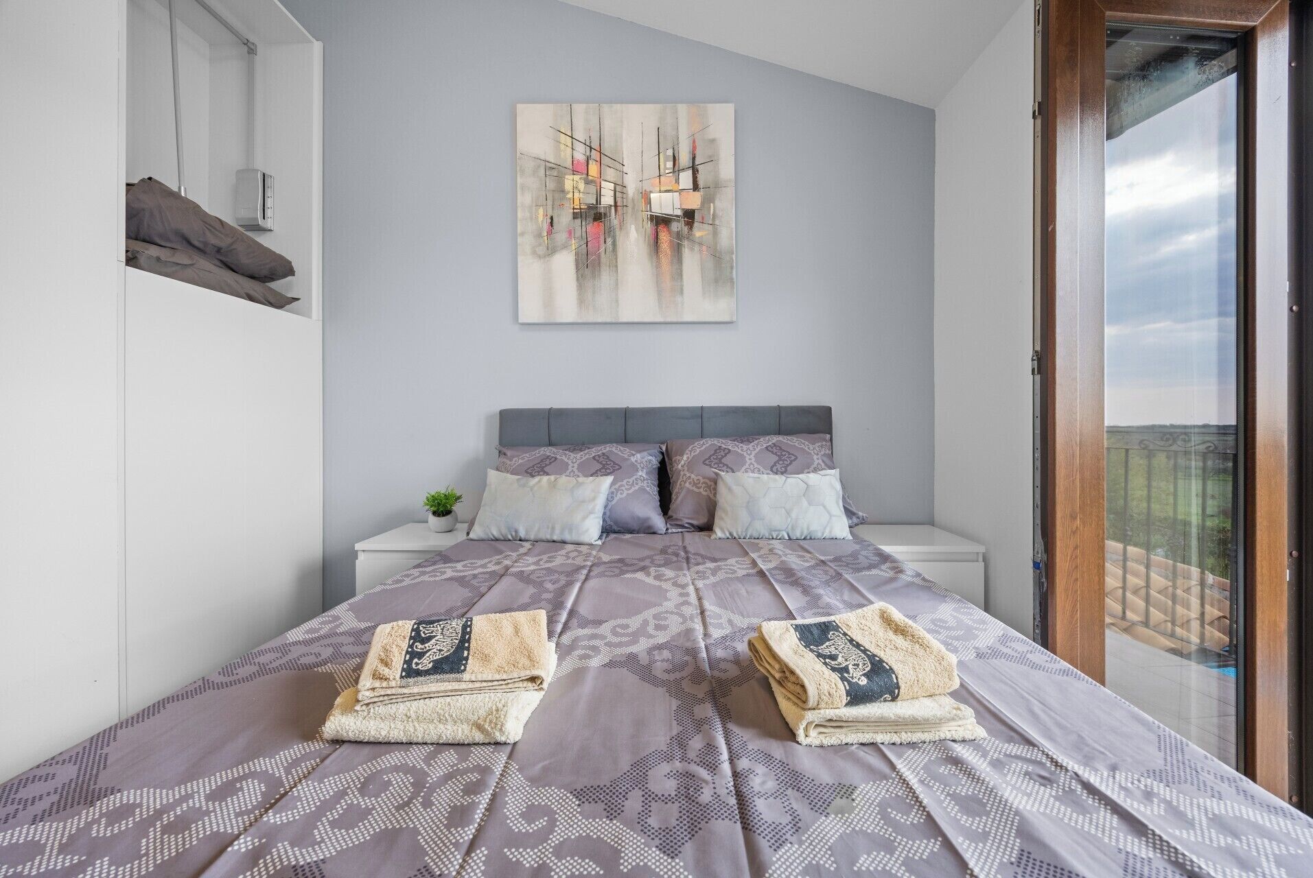 Ein Schlafzimmer mit einem Bett, Kissen, einem Nachttisch mit Pflanze und einem Bild an der Wand.