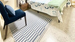 A bedroom with a bed, a chair, a bedside table, an air conditioning unit, and a window with curtains. - Una Casita Acogedora en Tenares (Tenares)