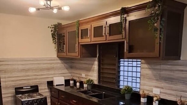 A kitchen with wooden cabinets, a black countertop, a gas stove, and a window with a view. - Una Casita Acogedora en Tenares (Tenares)