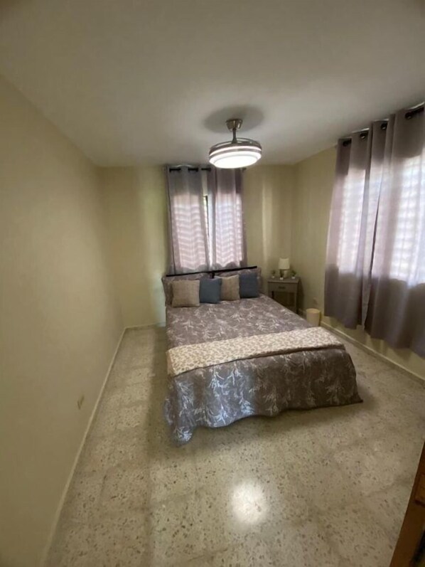 Une chambre à coucher avec un lit, des rideaux, une table de chevet et un luminaire au plafond.