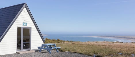 A small white building with a door and a window, a picnic table, and a view of the ocean.