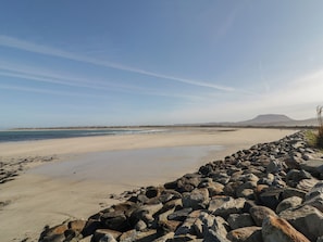 Een strand met een rotsachtige kustlijn, een heldere lucht en heuvels in de verte.