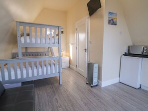 Una habitación con literas, un radiador blanco, una kitchenette pequeña y una puerta que da a otra estancia.