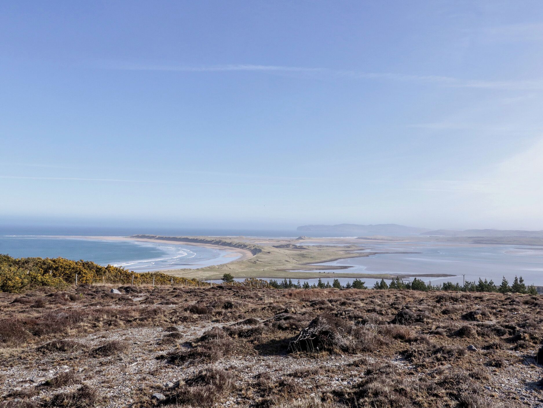 Un paysage côtier avec une plage, des dunes et un ciel dégagé.