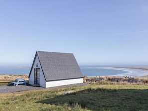 Een klein, wit, gelijkvloers gebouw met een schuin dak, gelegen op een grasachtige heuvel met uitzicht op een strand en de oceaan.
