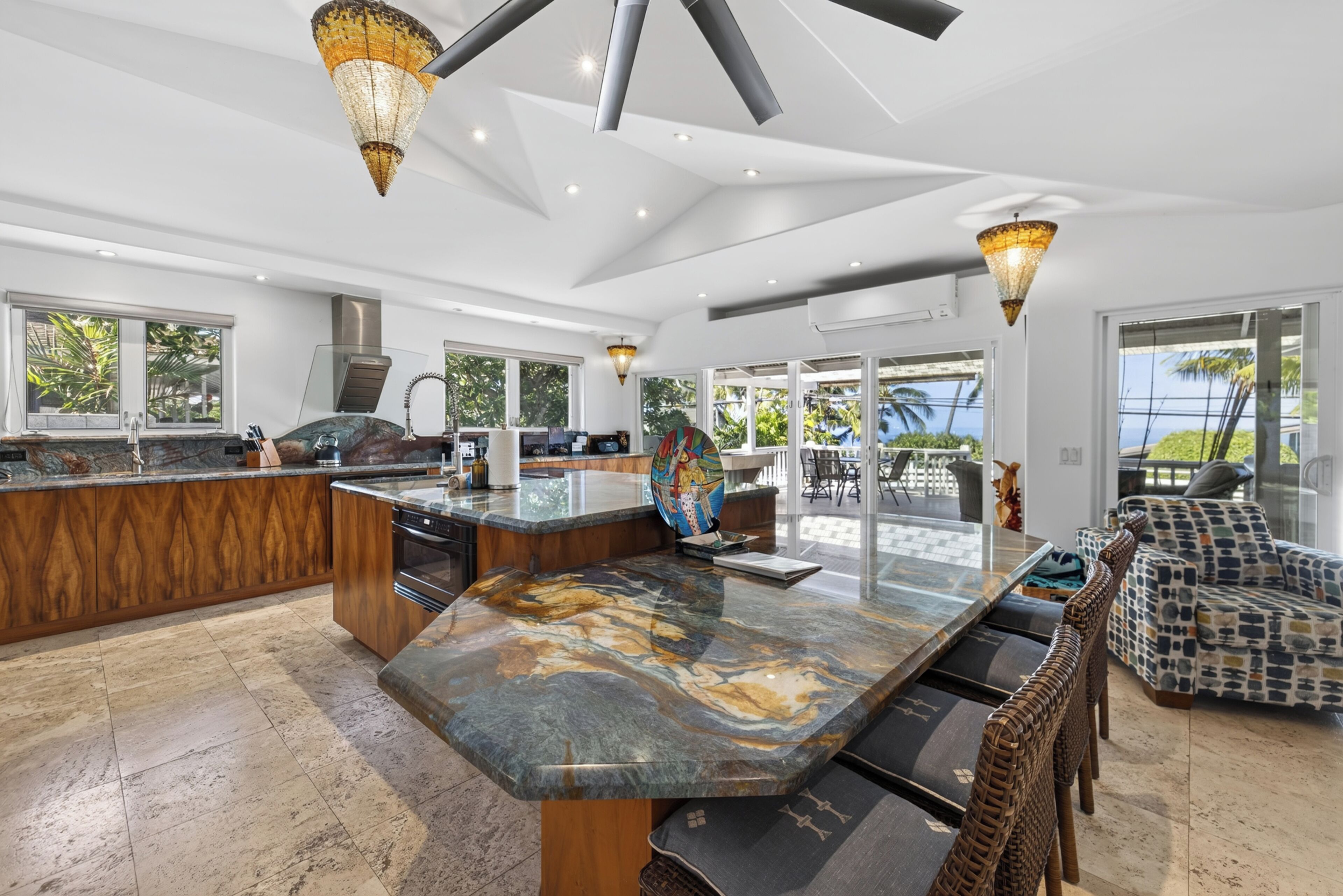 A spacious kitchen with a large island, modern pendant lights, and a view of the outdoors through large windows.