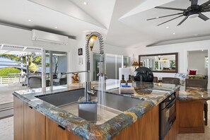 A modern kitchen with a marble countertop, a built-in dishwasher, and a ceiling fan. -    🌴Hale Honu | AC | Ocean Views | Renovated Master | A Diver's Paradise Awaits🌴 (Kailua Kona)