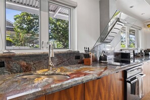 A modern kitchen with a marble countertop, stainless steel appliances, and a view of greenery outside. - 🌴Hale Honu | AC | Ocean Views | Renovated Master | A Diver's Paradise Awaits🌴 (Kailua Kona)