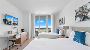 Een hotelkamer met een bed, bureau, stoel en een groot raam met uitzicht over de stad.