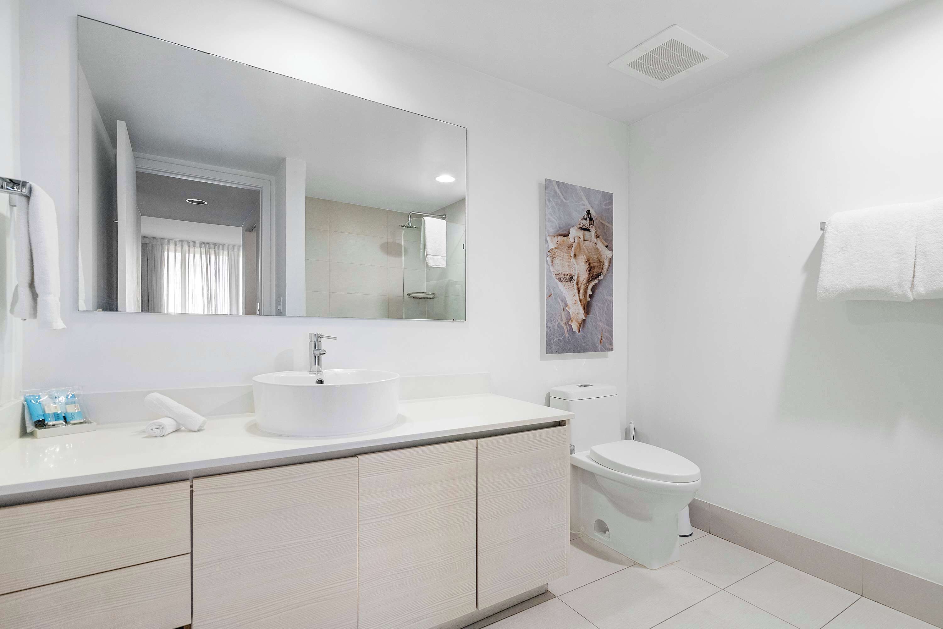 A modern bathroom with a large mirror, white sink, toilet, and a shower area.