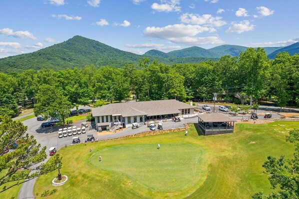 Un parcours de golf doté d ’un club-house, d’un parking et entouré de verdure.
