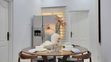 En matplats med ett runt bord, fyra stolar, ett kylskåp och en dörr med en lampa.