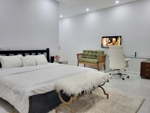A modern bedroom with a large bed, a desk, a chair, and a television.
