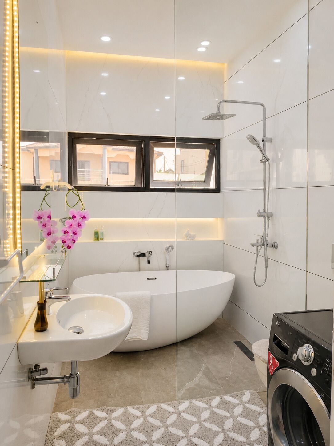 A modern bathroom with a freestanding bathtub, a shower, a washing machine, and a window with a view.