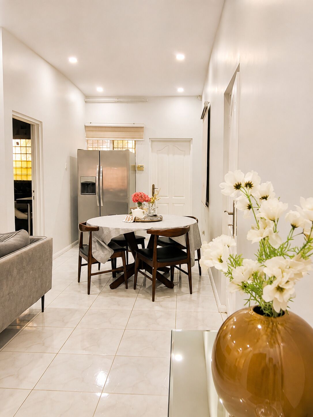 A modern kitchen with a dining area, a refrigerator, and a vase with flowers.