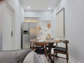 A compact room with a dining table, chairs, a refrigerator, and a door.